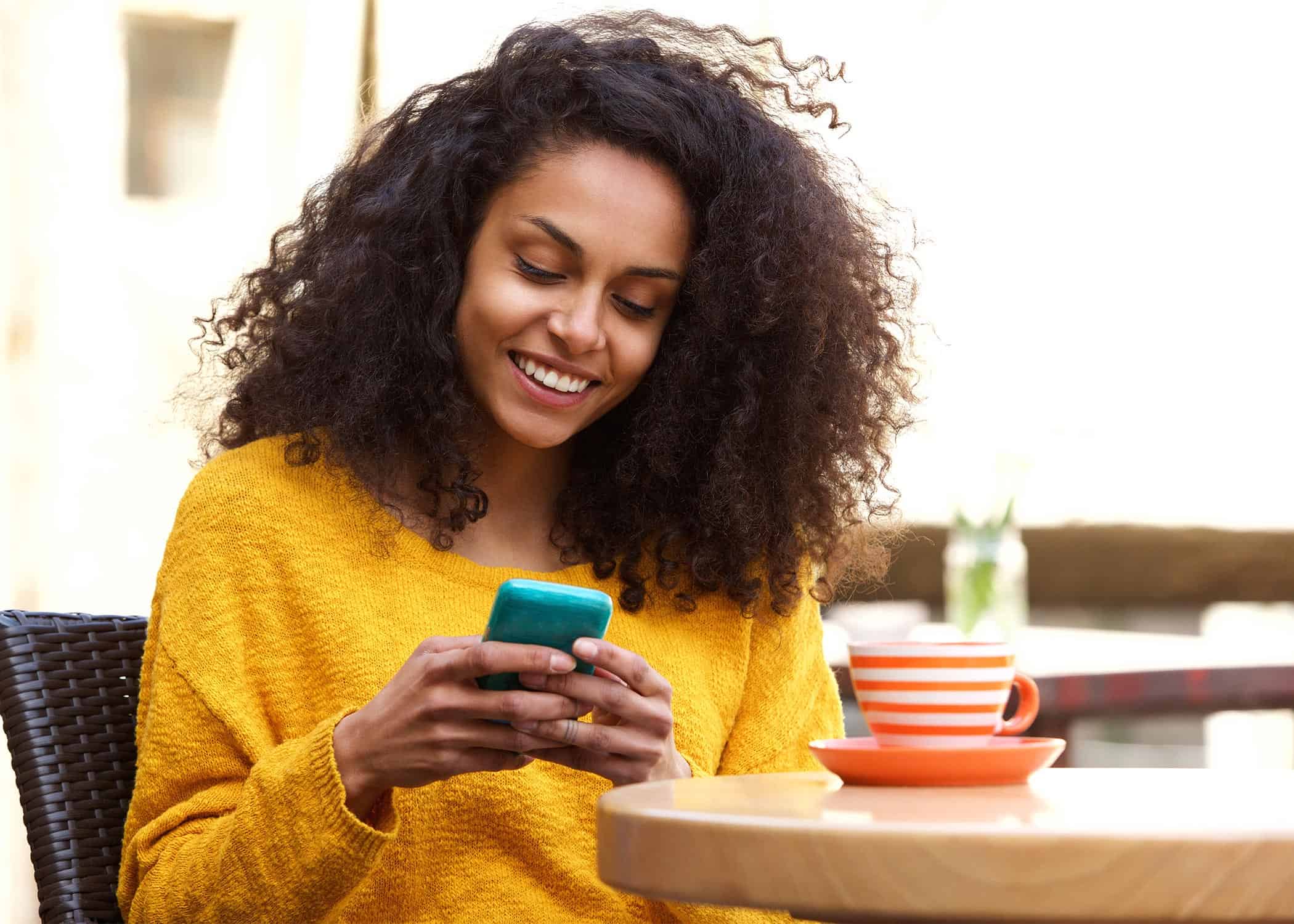 Beautiful-young-black-woman-reading-social-media-cell-phone-at-coffee-shop