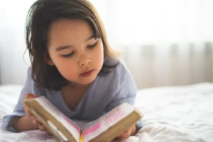 teaching your child about God. Little girl laying on a bed reading a bible