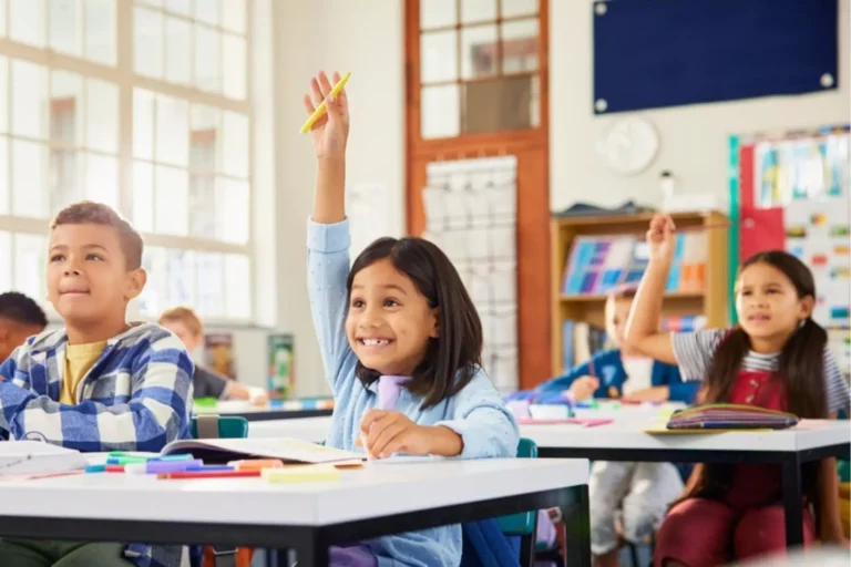 Little girl with big grin raising her hand in school