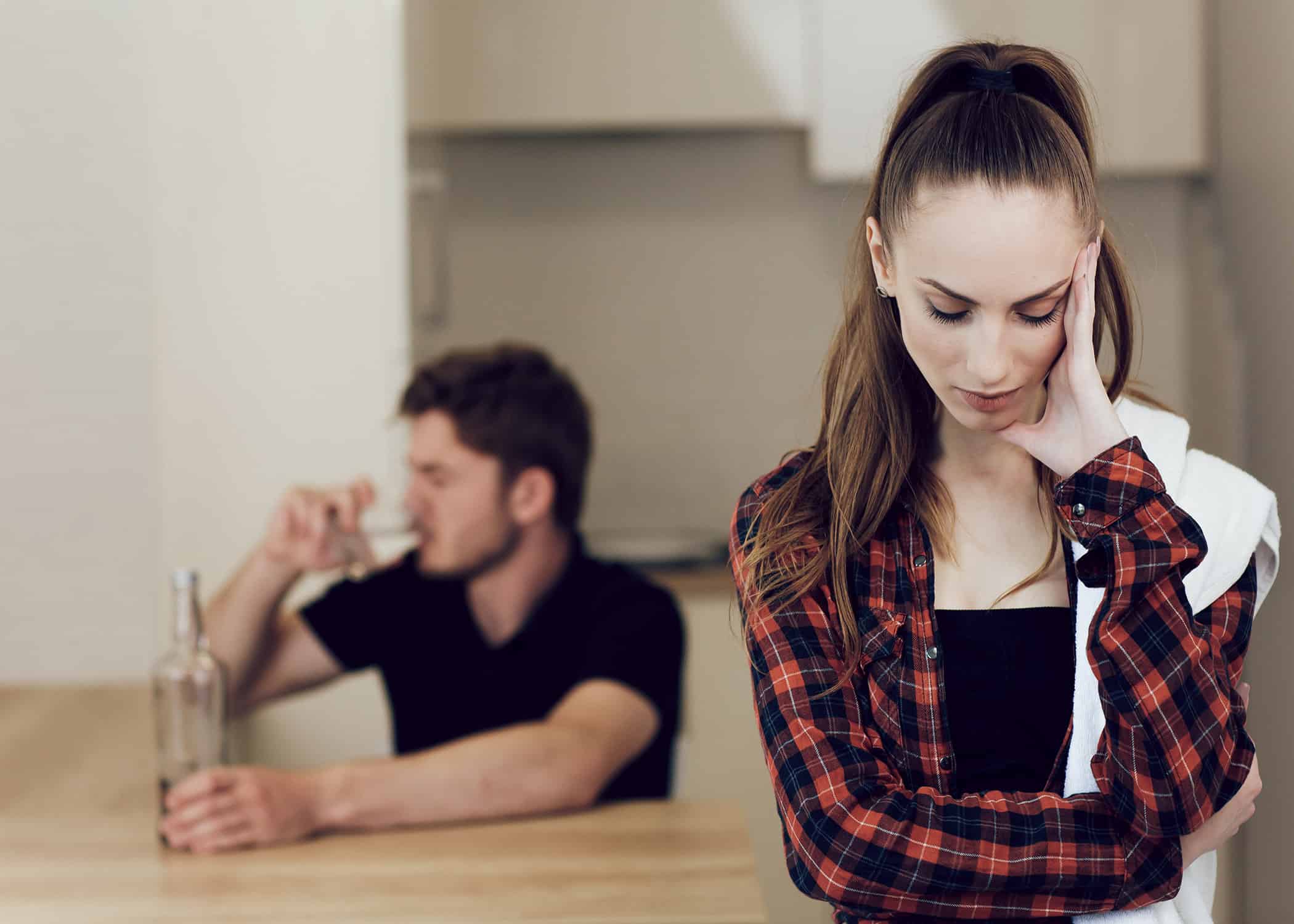 Upset-woman-who-is-spouse-of-an-addict-with-drunk-husband-in-background