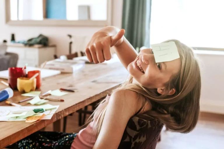 Little girl with her thumbs up and a sticky note on her forehead.