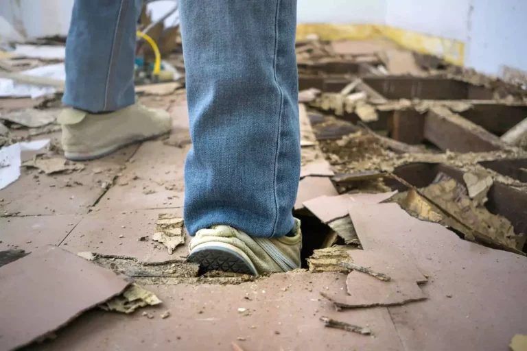 A close-up of a person’s foot breaking through a damaged wooden floor, symbolizing the struggles and challenges in learning how to fix a broken marriage.