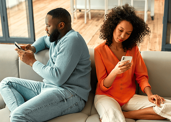 Black-married-couple-sitting-on-sofa-with-phones-facing-away-from-each-other.