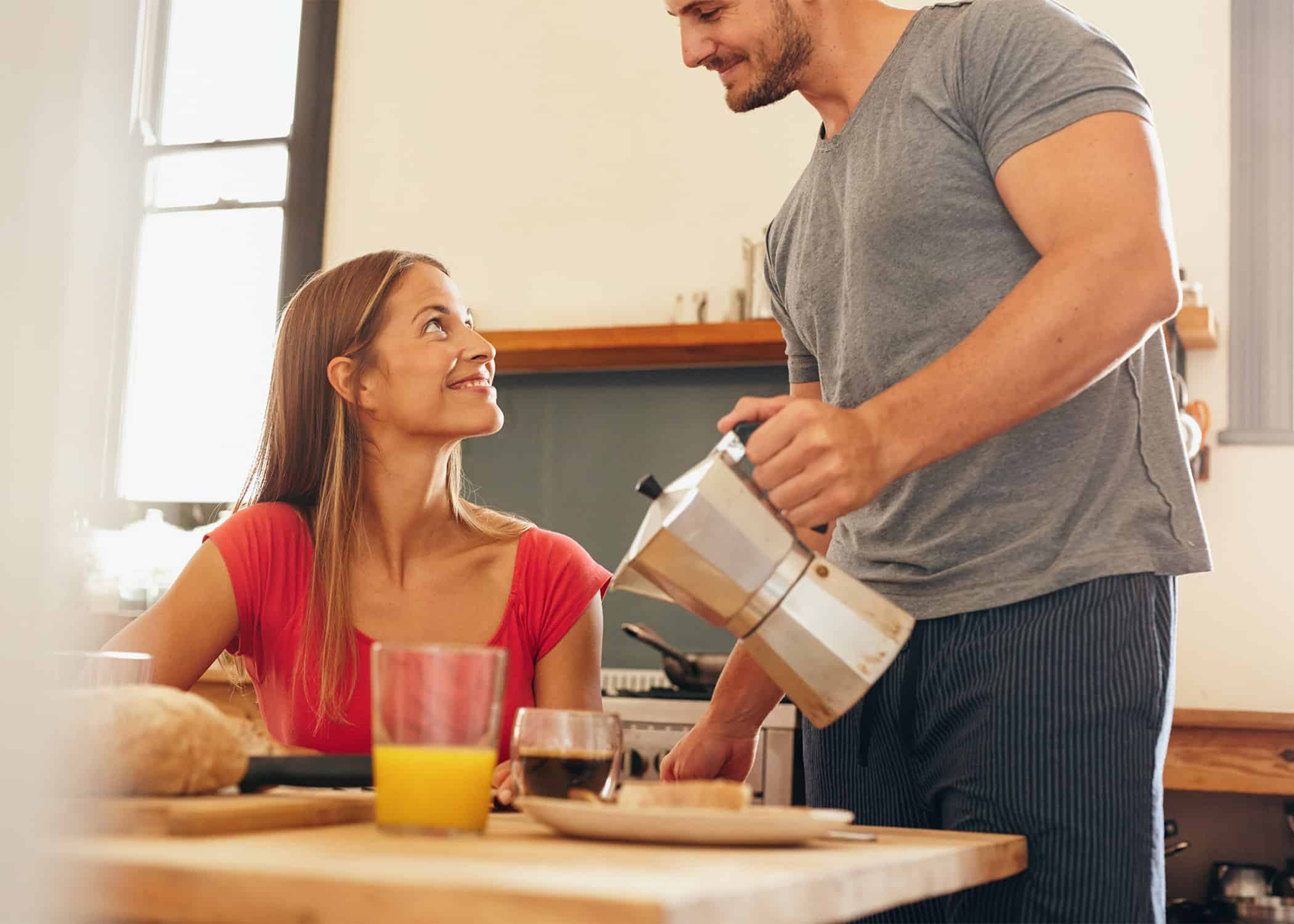 Husband-standing-and-pouring-coffee-for-wife-at-breakfast-while-she-sits-at-table