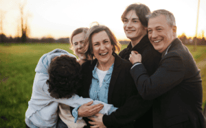 sharing moments with our children - Fun Loving Family Hugging Together Outside. They are laughing and close enjoying evening sunset in field together.