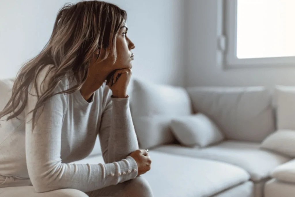 Young adult woman sitting pensively on couch and staring out the window