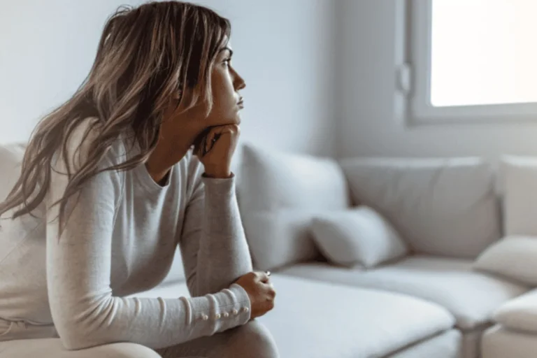 Young adult woman sitting pensively on couch and staring out the window