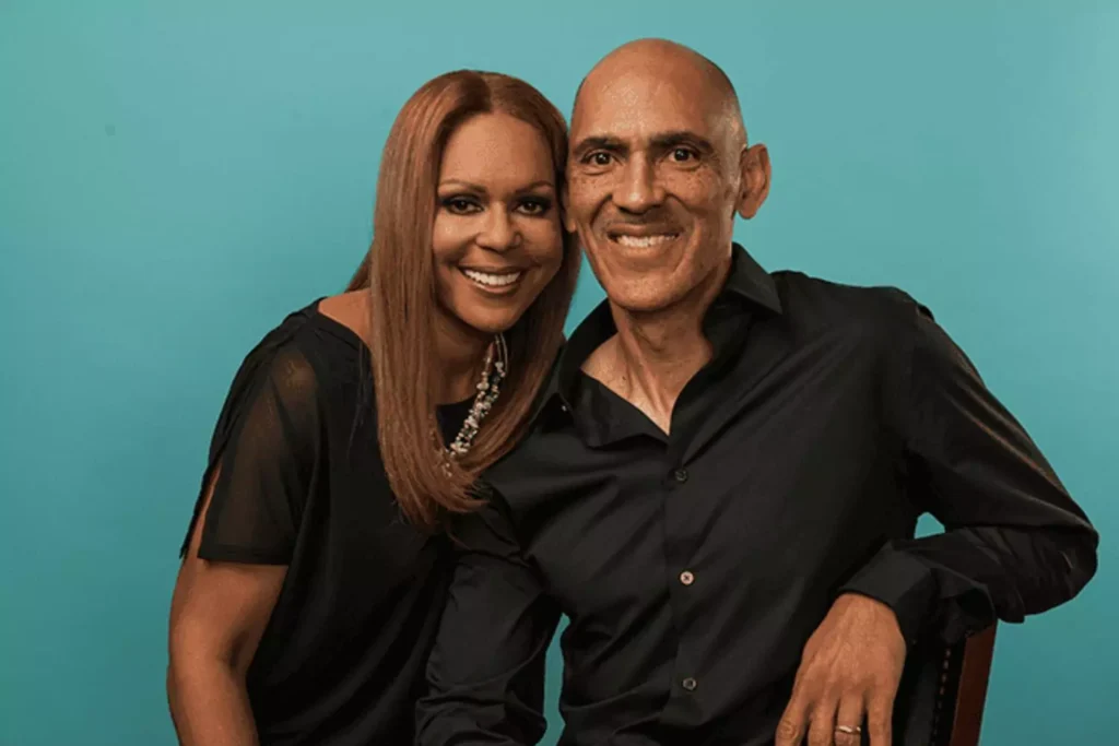 Lauren and Tony Dungy pose together against a teal background, both smiling warmly. Their expressions and body language reflect a strong, loving partnership built on mutual respect, shared values, and great teamwork.