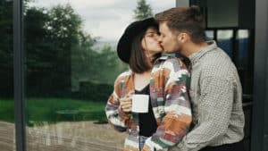 Young-married-couple-kissing-in-morning-outside-house-wife-holding-coffee-cup