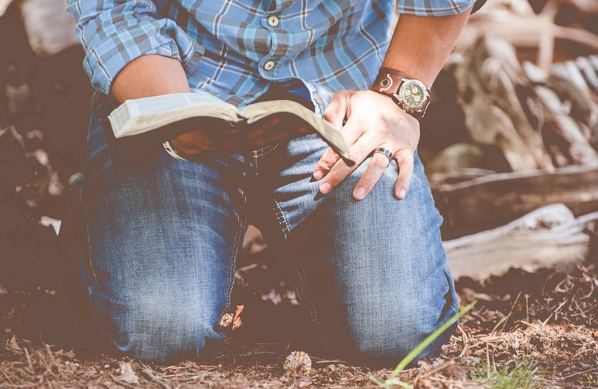 Photo of a pastor kneeling on the ground with Bible