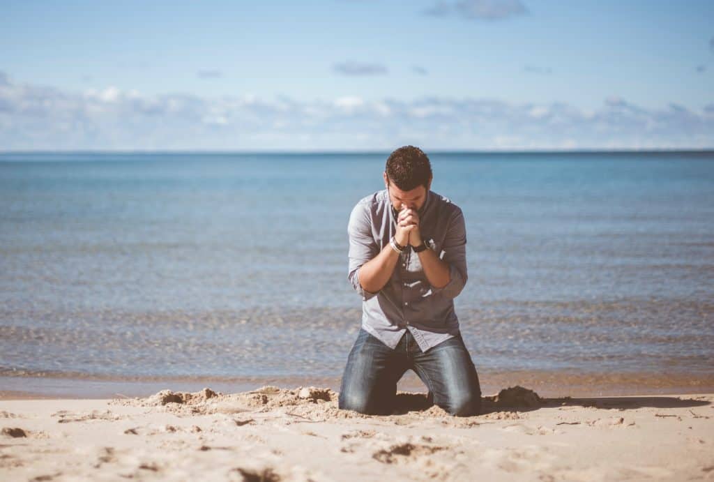 Photo of man kneeling on beach, praying.