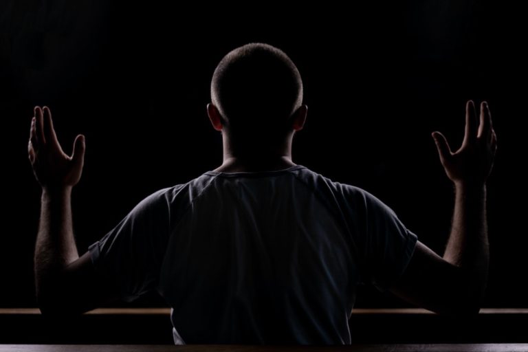 Photo of a man praying in the dark, hands lifted in the air.