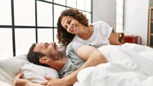 Middle-aged-woman-smiling-at-her-older-husband-lying-in-bed