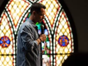 Pastor preaching in front of stained glass at his church.