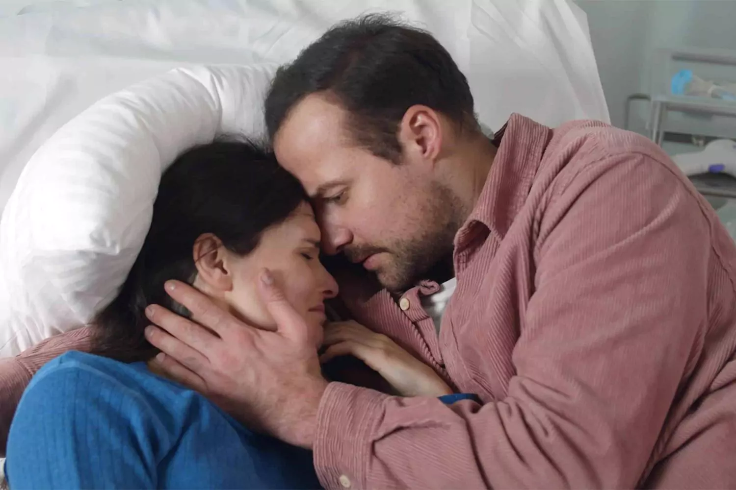 A man tenderly embraces his wife in a hospital bed, offering comfort during a deeply emotional moment, representing the journey of when your spouse has a terminal illness.