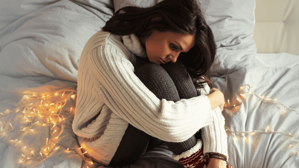 Coping with Christmas, young woman sitting on her bed with Christmas lights around her dealing with grief