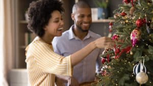 Content-mixed-race-husband-and-wife-putting-ornaments-on-Christmas-tree
