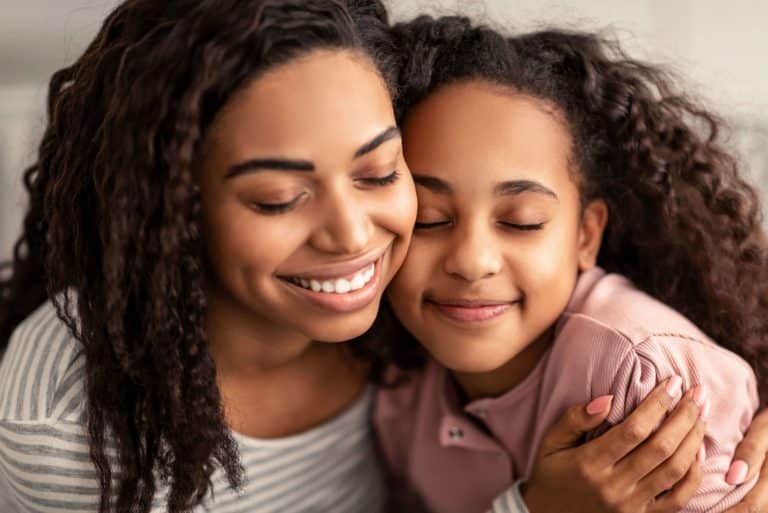 Close-up of smiling African-American mom side-hugging your tween daughter