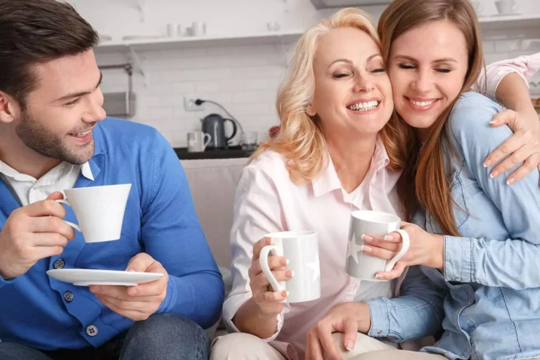 A couple sitting on the couch with his mother who is hugging his wife