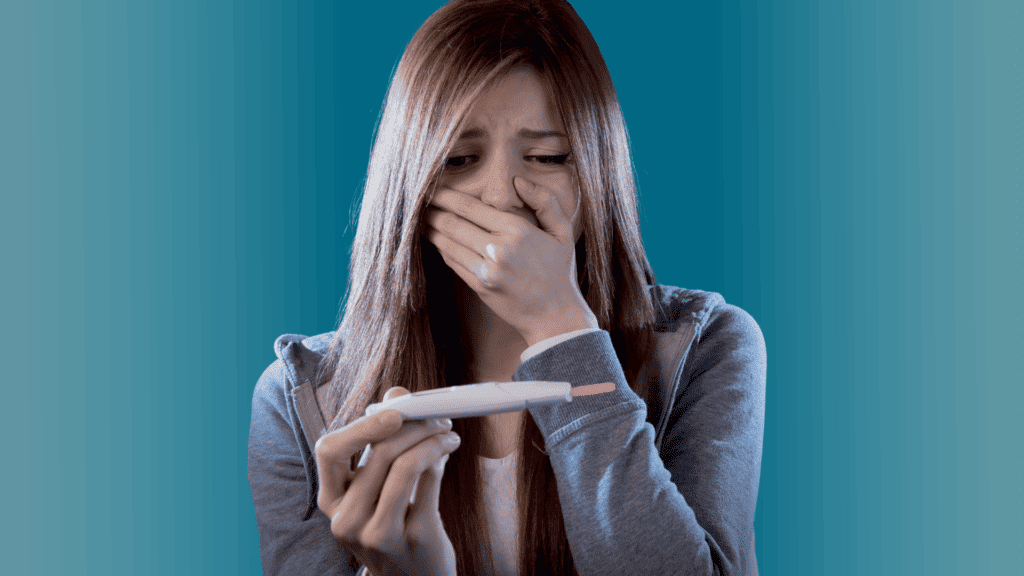 a pregnant teenager, young girl holding a pregnancy test in one hand, her other hand is over her mouth in fear of the results.