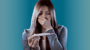 a pregnant teenager, young girl holding a pregnancy test in one hand, her other hand is over her mouth in fear of the results.