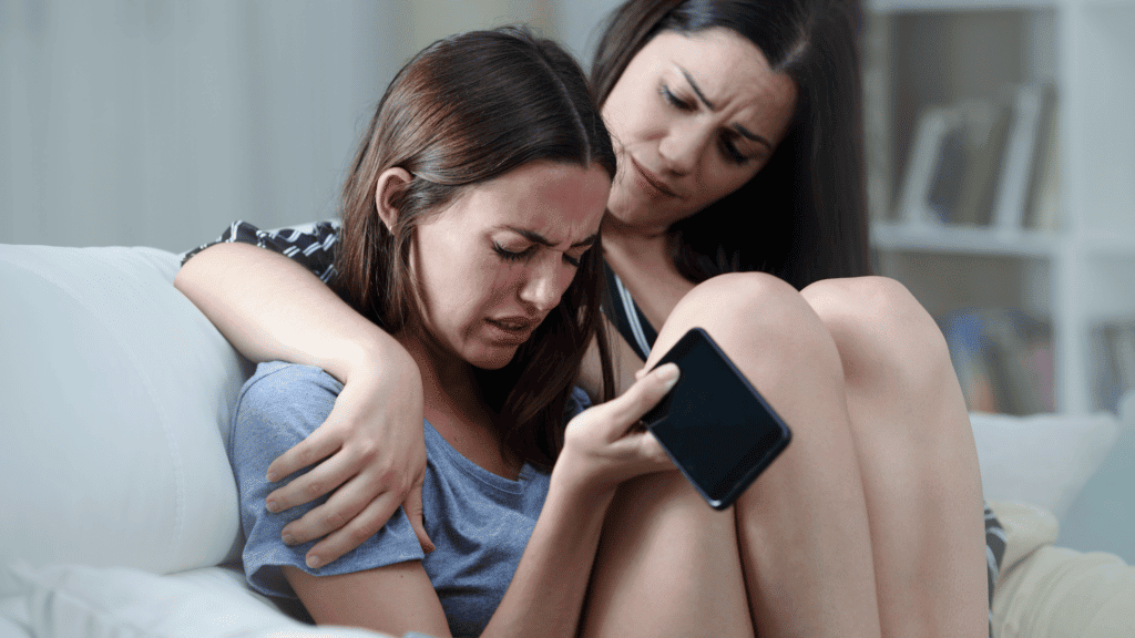 Anxiety ridden teenaged girl, holding a phone, being comforted by her mother.