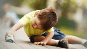 Raising little boys is different than raising girls. Little boy about two years old sitting on a deck playing with his toy car.