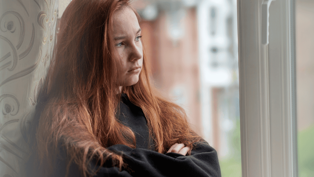 Moody teen, teenaged redheaded girl sitting with her arms crossed.