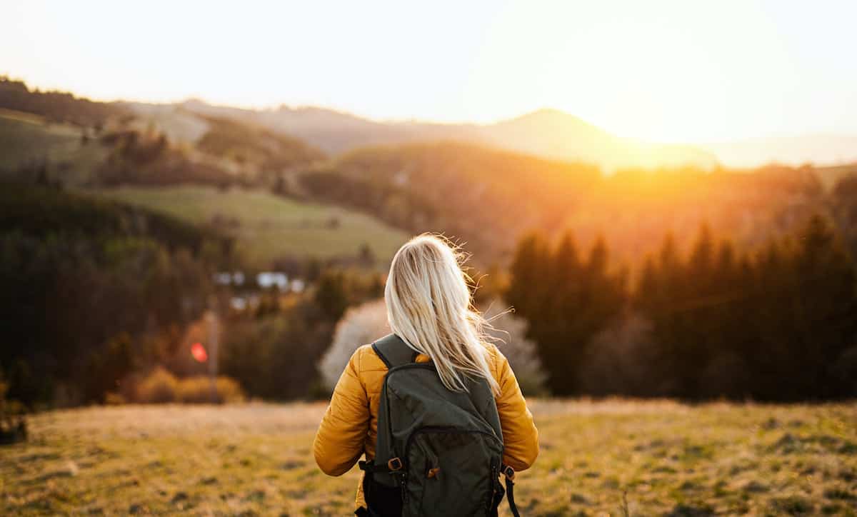 A rear view of senior woman walking outdoors in nature at sunset, hiking.