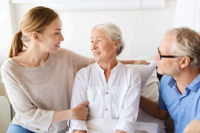 A loving daughter and her father sit beside an elderly mother, smiling and offering support, symbolizing the importance of caregiving for parents.