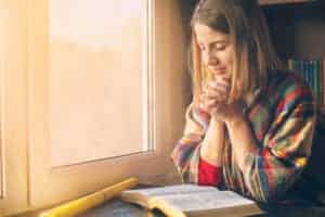 Beautiful woman praying having the Bible opened in front of her.