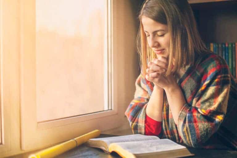 Beautiful woman praying having the Bible opened in front of her.