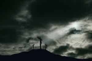 A depiction of the crucifixion of Jesus Christ on a cross with 2 other robbers nearby on Calvary. The sky is darkened and rays of light break through the clouds onto the cross for drama. Concept of the death of Jesus on Good Friday and His resurrection on Easter Sunday. Horizontal orientation with copy space.