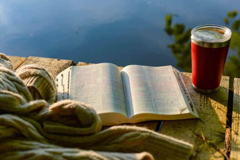 Photo of an open bible and a coffee on a table in the sunlight.