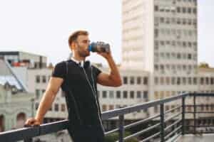 Young man resting on the roof of the building after workout and drink water