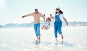 Playing parents and girl in water at beach for bonding, quality time and summer adventure together. Travel, family and happy mom and dad swinging child enjoy holiday, vacation and relax on weekend.