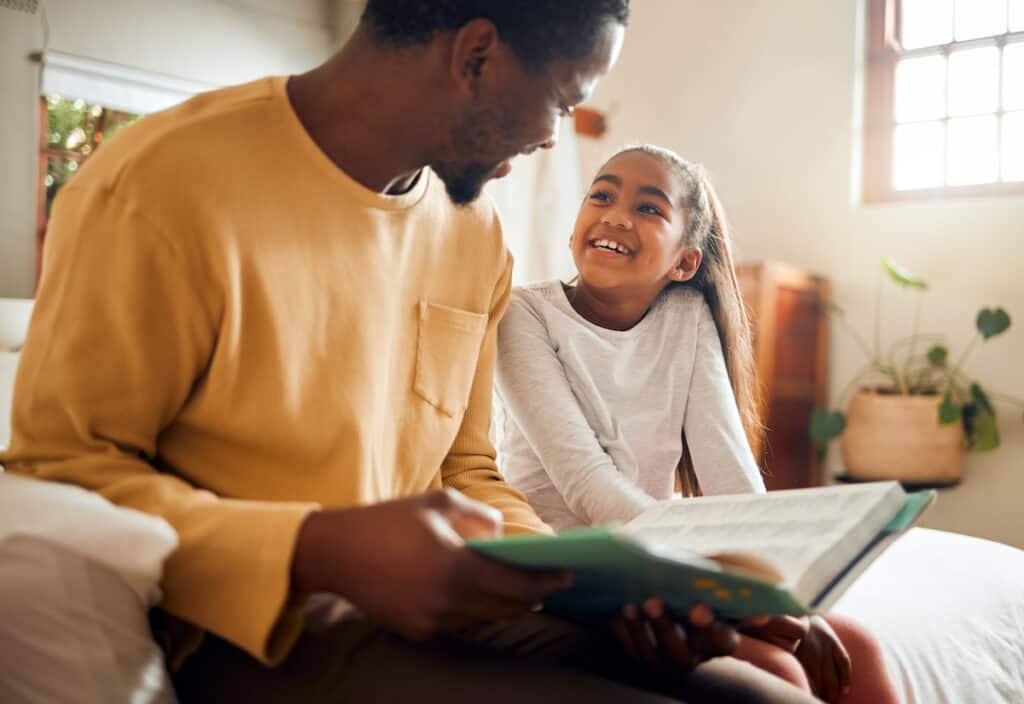 Father, child and book for story time on bed with smile enjoying reading or listening and bonding together at home. Happy dad and daughter sitting with textbook for learning or education in bedroom.