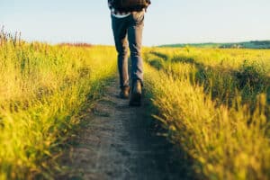 Active tourist, a man with a briefcase in nature, a hipster in a cap is walking along a path on a green hill, healthy lifestyle, nature, rest