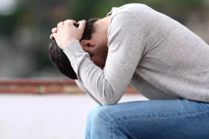 Adult man grieving with his head down, sitting on a bench