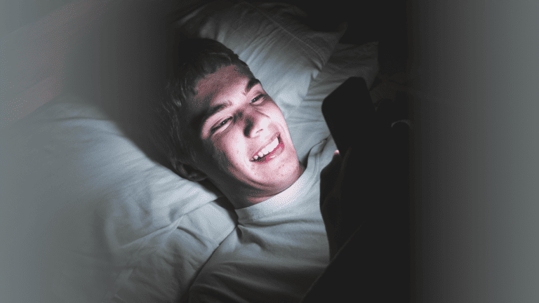 Teen watching his phone, at night in bed not sleeping.