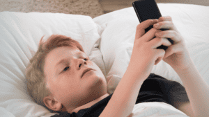 building trust with your teens in a digital age. Teenage boy laying on his bed looking at his phone.