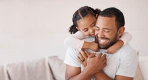 Kid hugging dad in lounge for happy fathers day, love and care while relaxing, bonding and funny play at home. Mockup with excited girl child, smile parent man and laughing family happiness together.