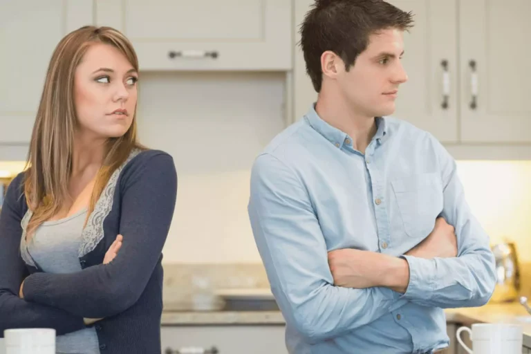 Married couple standing with their backs to each other with arms crossed. The woman looks over her shoulder at the man, wondering how to apologize to her spouse.