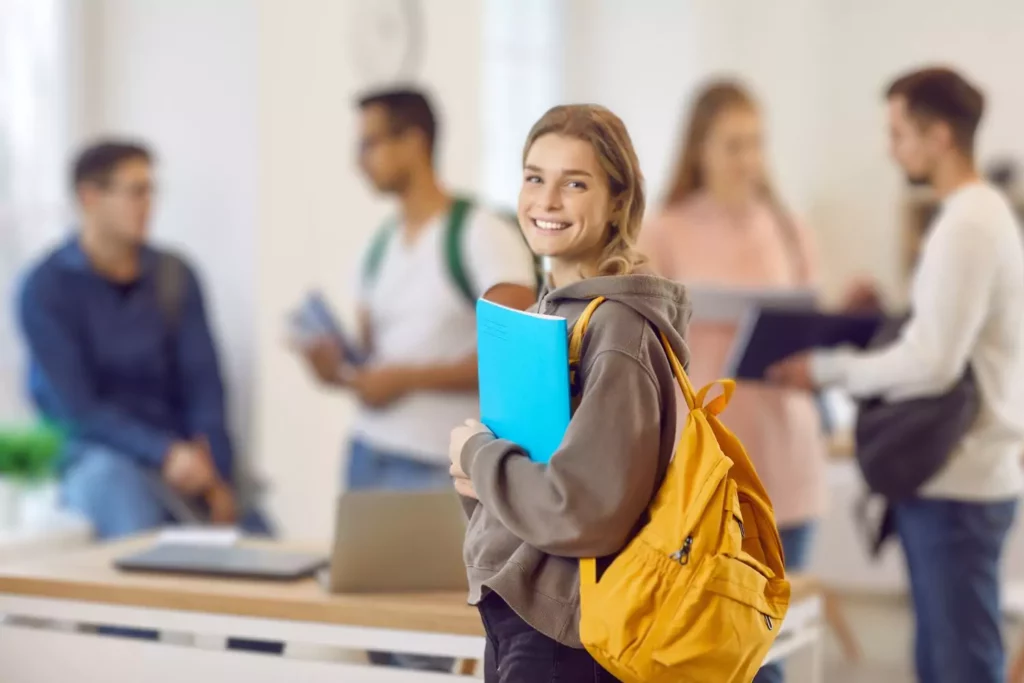 Homeschooled girl on her first day of college. Smiling at the camera, with classmates in the background