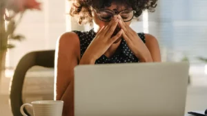 A bride-to-be sits at her laptop with her head in her hands, anxious about her wedding finances.