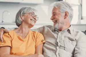 A mature, empty nest couple sit on a couch and look adoringly into each other's eyes.