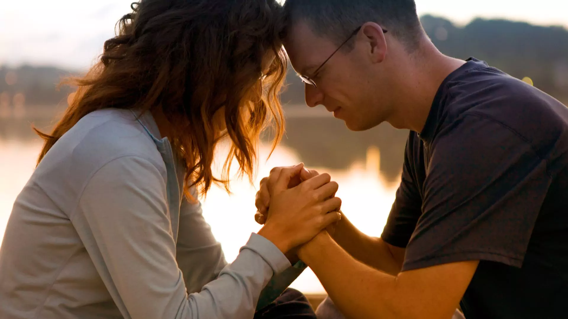 A man and woman with their heads together, holding hands, and seeking spiritual unity in their marriage.