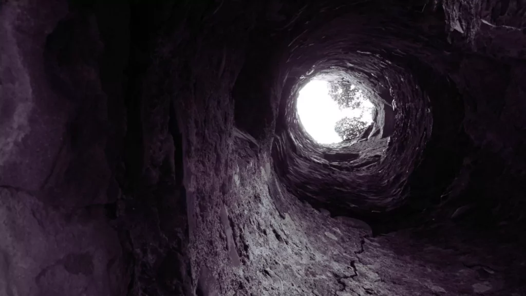 You are underground, in a dark hole, looking up at the light, far above you.