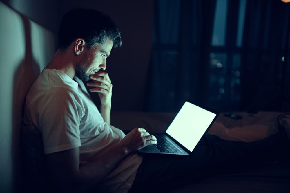 A man looking intently at a laptop in a dark room