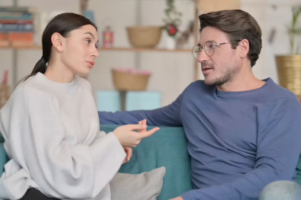 A woman and a man sit on a couch having an open-hearted discussion to resolve conflict.